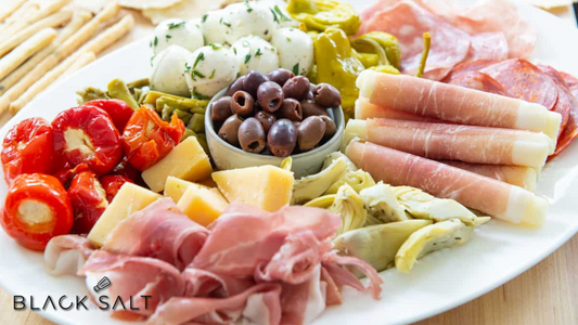 An enticing assortment of cured meats, marinated vegetables, cheeses, and olives, beautifully arranged on a platter for a vibrant and flavorful antipasto experience.